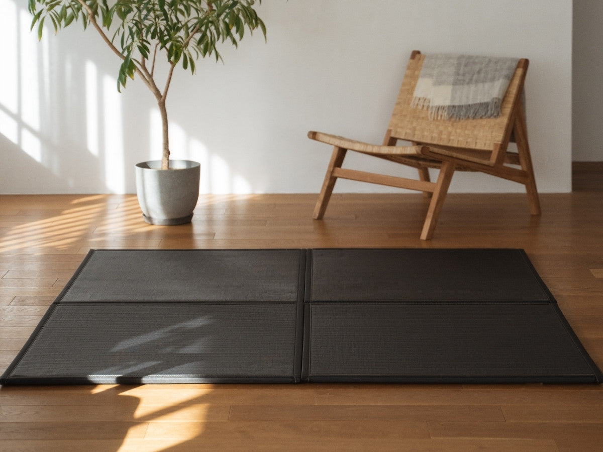 Vier schwarze Tatami-Matten in Einheitengröße, die auf einem Wohnzimmerboden als moderner und langlebiger Zen-Deko-Teppich angeordnet sind.