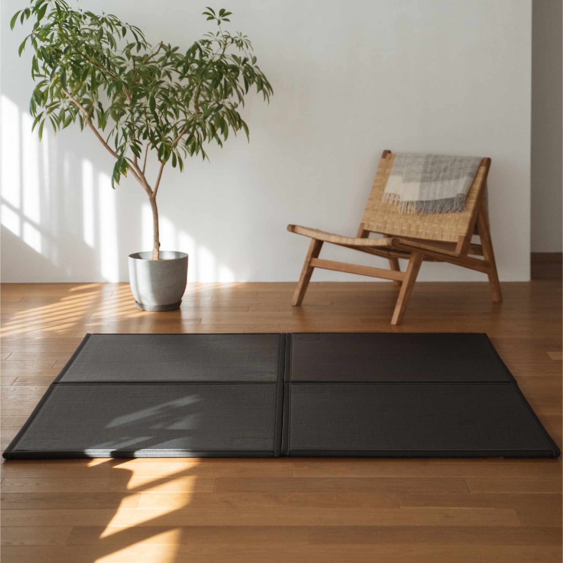 Vier schwarze Tatami-Matten in Einheitengröße, die auf einem Wohnzimmerboden als moderner und langlebiger Zen-Deko-Teppich angeordnet sind.