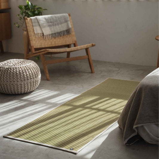 Natural rush grass tatami yoga mat laid on a concrete living room floor serving as a minimalist zen decor runner.