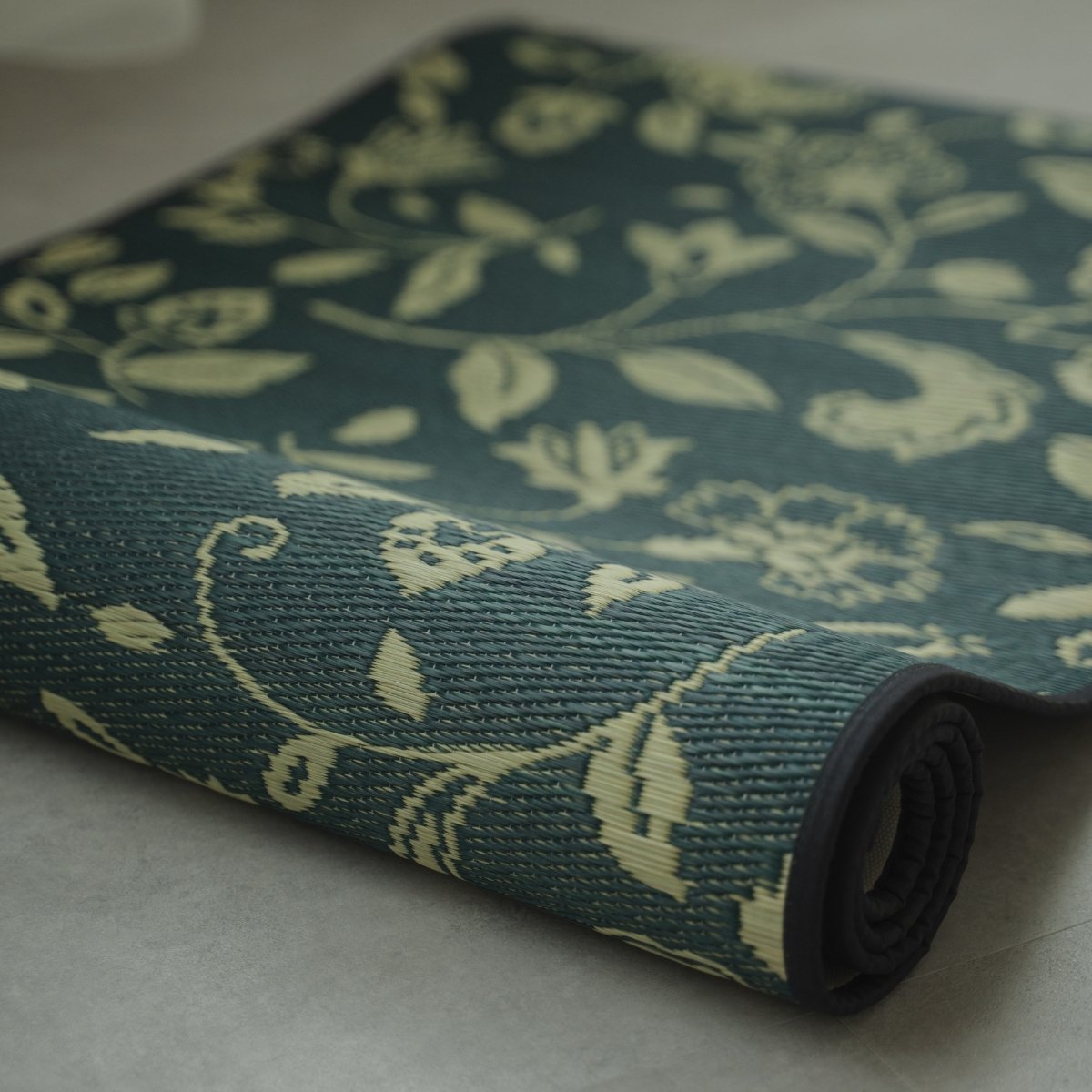 Japanese Tatami Yoga Mattress "Sarasa" Navy partially rolled on a grey floor, showcasing the natural rush grass weave and pattern.