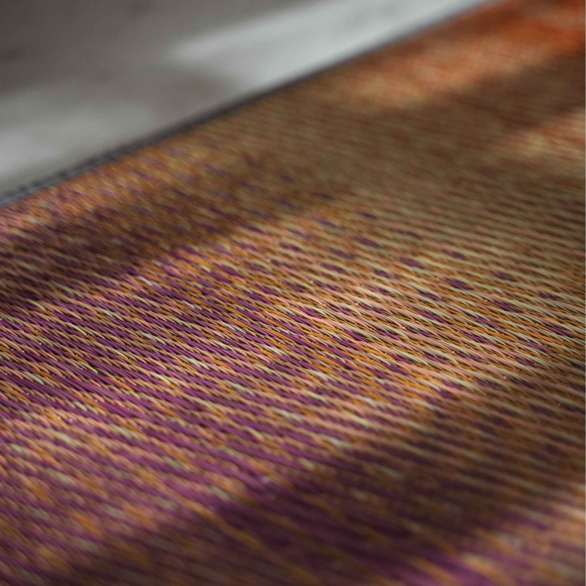Nahaufnahme von geflochtenem Binsengras auf einer roten Tatami-Matte, die den Farbverlauf des Sonnenuntergangs zeigt.
