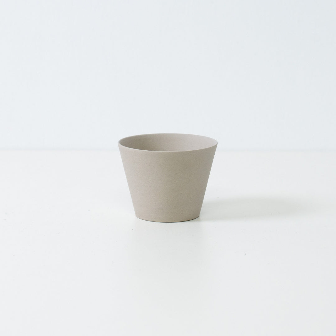 Minimalistisk hvid japansk teacup i ensui kegleform lavet af uglaseret stentøj, der står på et hvidt bord.