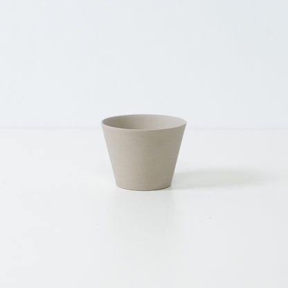 Minimalistisk hvid japansk teacup i ensui kegleform lavet af uglaseret stentøj, der står på et hvidt bord.
