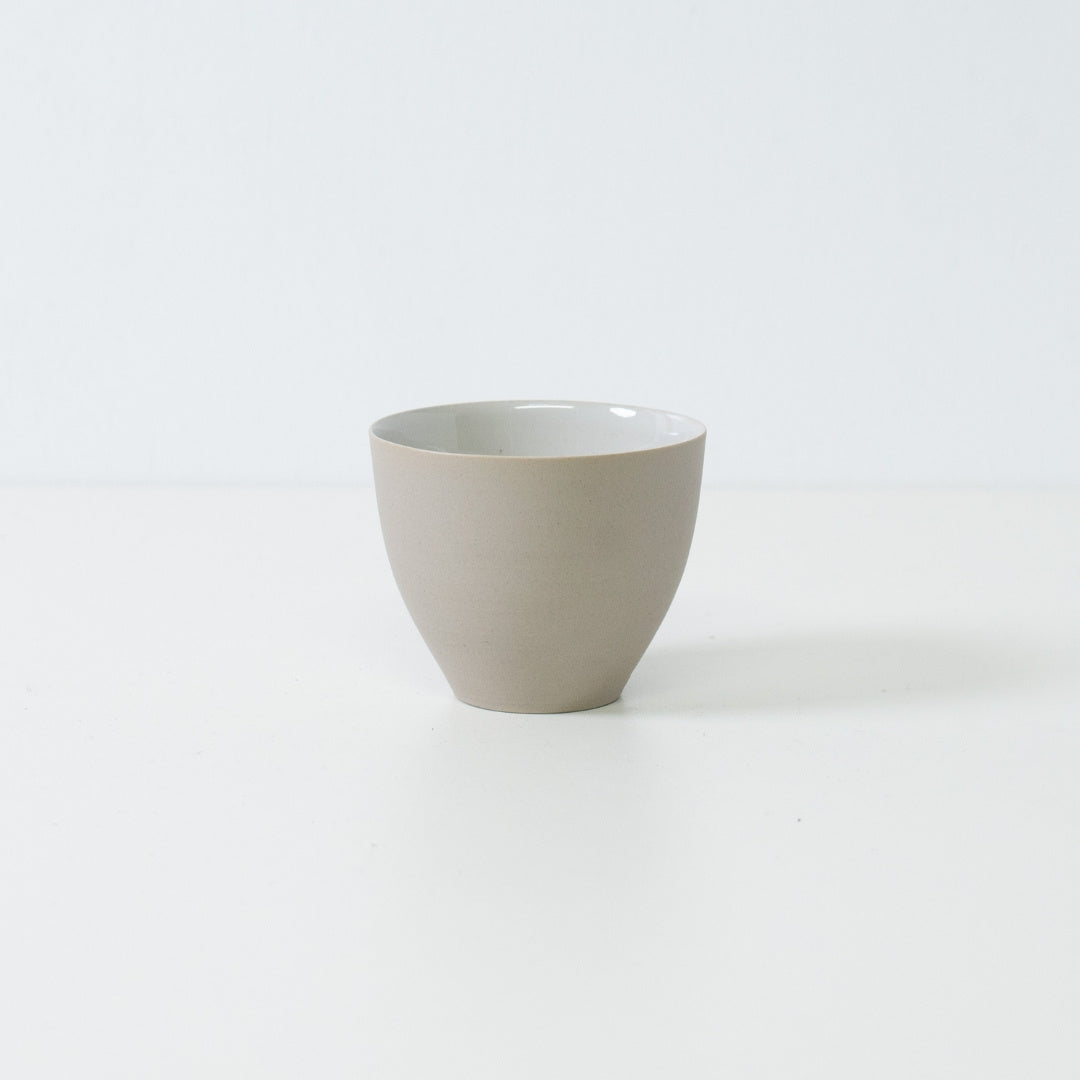Sidevisning af en enkelt moderne f-formet japansk teacup, der viser dens buede, uglacerede hvide yderside og stabile bund