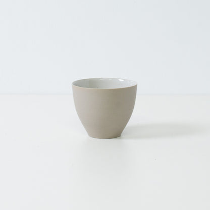 Sidevisning af en enkelt moderne f-formet japansk teacup, der viser dens buede, uglacerede hvide yderside og stabile bund