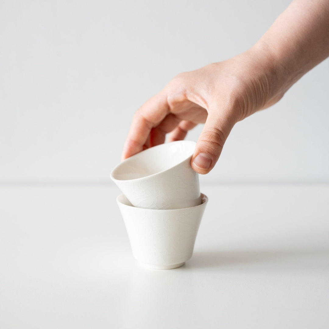 hånd, der stabler to hvide japanske tekopper, som viser det høje foddesign og den unikke Kannyu-krakelerede glasurtekstur.