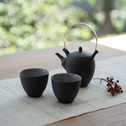 Service à thé japonais noir avec kyusu sur une table en bois pour les amateurs de thé profitant d'un rituel zen moderne.