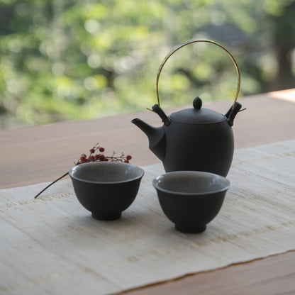 Théière japonaise noire « Donguri » et tasses à thé japonaises sur un chemin de table en lin pour les amateurs de bien-être se relaxant avec du thé.