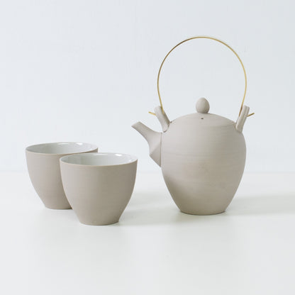 Moderne japansk tesæt med en hvid ler kyusu tekande med messinghåndtag ved siden af to buede tekopper i f-form