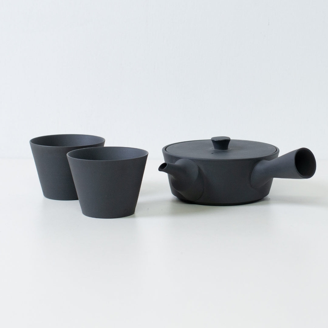 Moderne sort japansk tesæt med en flad sencha kyusu tekande og kegleformede tekopper på et hvidt bord