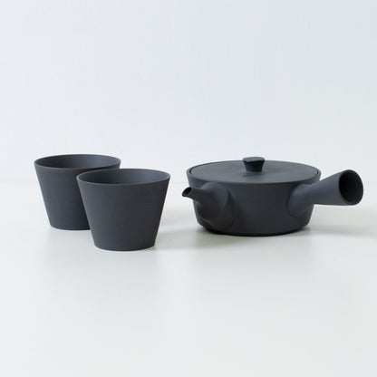 Moderne sort japansk tesæt med en flad sencha kyusu tekande og kegleformede tekopper på et hvidt bord