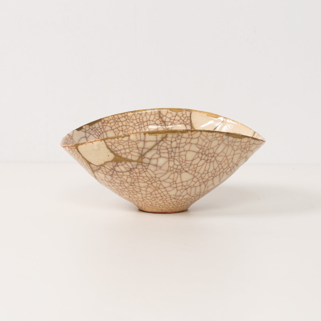 "Un bol kintsugi blanc fait à la main se dresse sur une table, exposant des lignes dorées d'art de poterie authentique"
