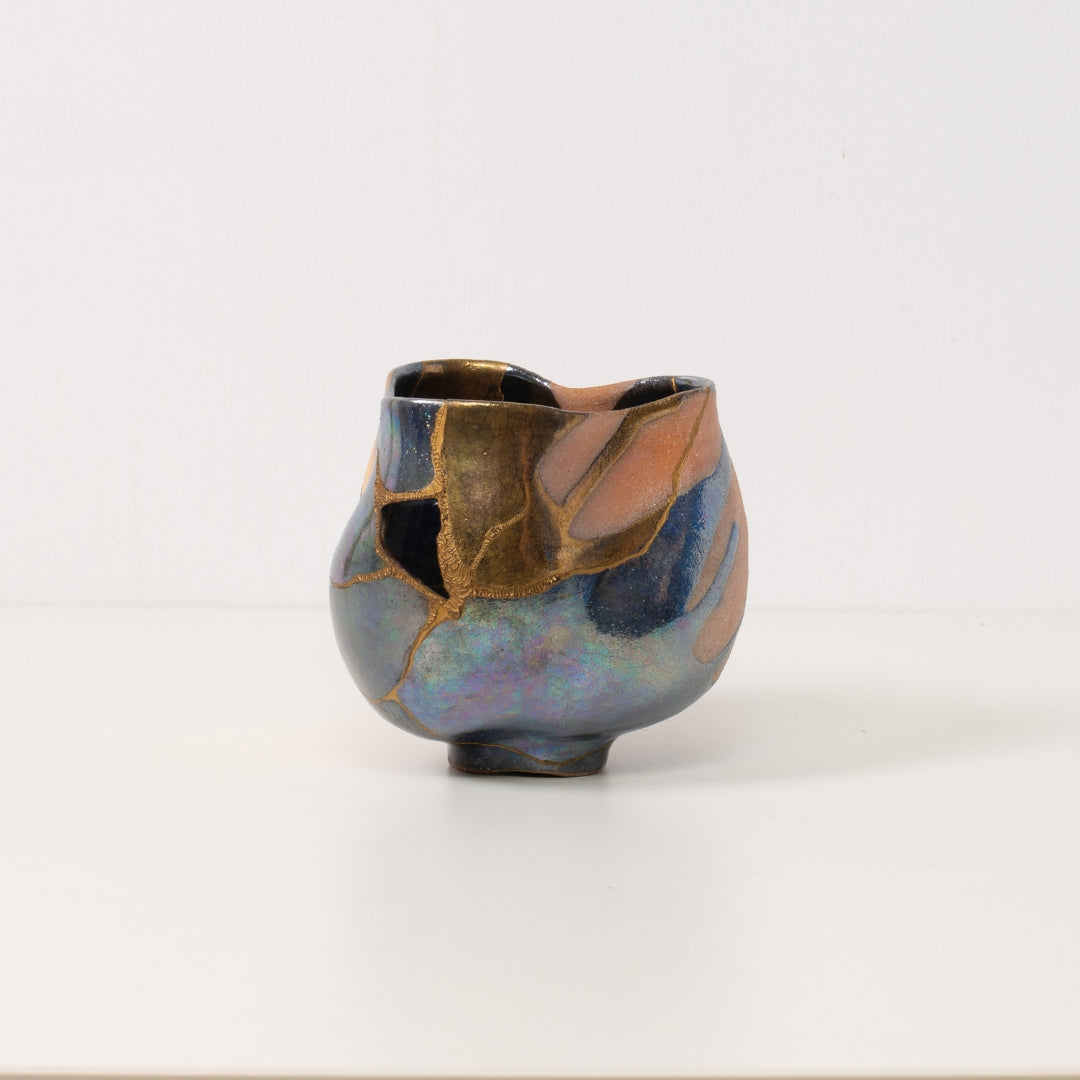 høj håndlavet kintsugi matcha-skål med farverige glasurer og gyldne reparationer står alene på et hvidt bord
