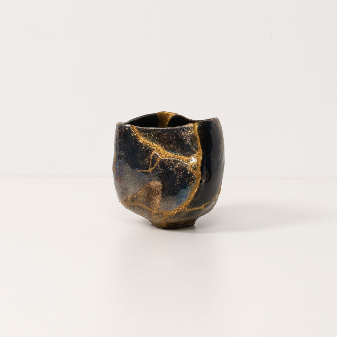 Eine schwarze Kintsugi-Matcha-Schale auf einem weißen Tisch mit goldenen Linien im Wabi-Sabi-Stil