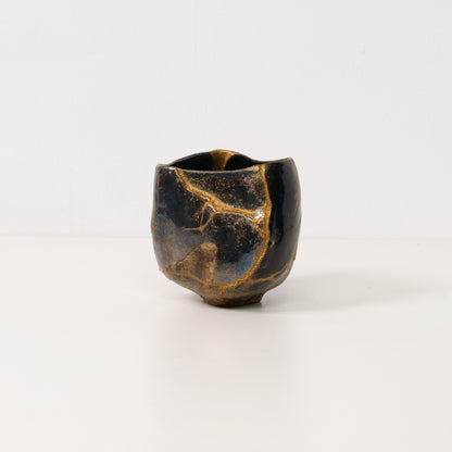 Eine schwarze Kintsugi-Matcha-Schale auf einem weißen Tisch mit goldenen Linien im Wabi-Sabi-Stil