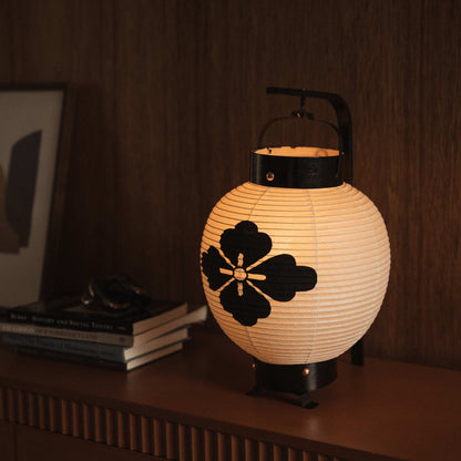 Gloeiende Japanse papieren lantaarn met een zwart bloem-diamant-embleemontwerp geschilderd op warm wit washipapier.