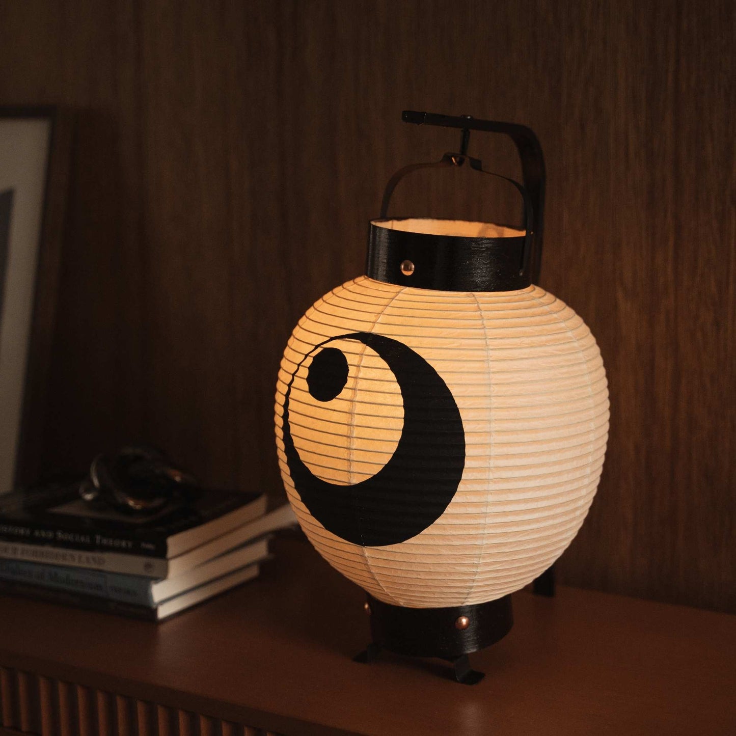 Kleine gloeiende Japanse papieren lantaarn met zwart maanontwerp op een houten oppervlak met warme washipapiertextuur