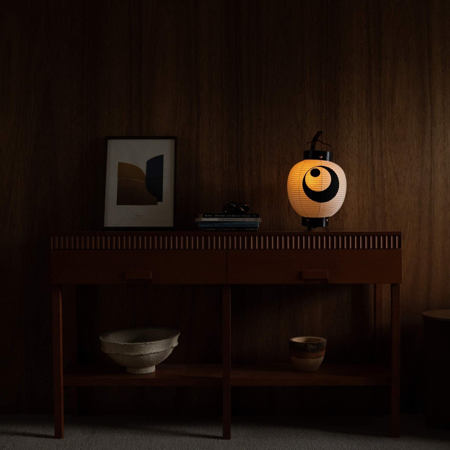 Lit Japanse papieren lantaarn staand op een mid-century modern dressoir die zorgt voor een warme sfeer in een woonkamer.