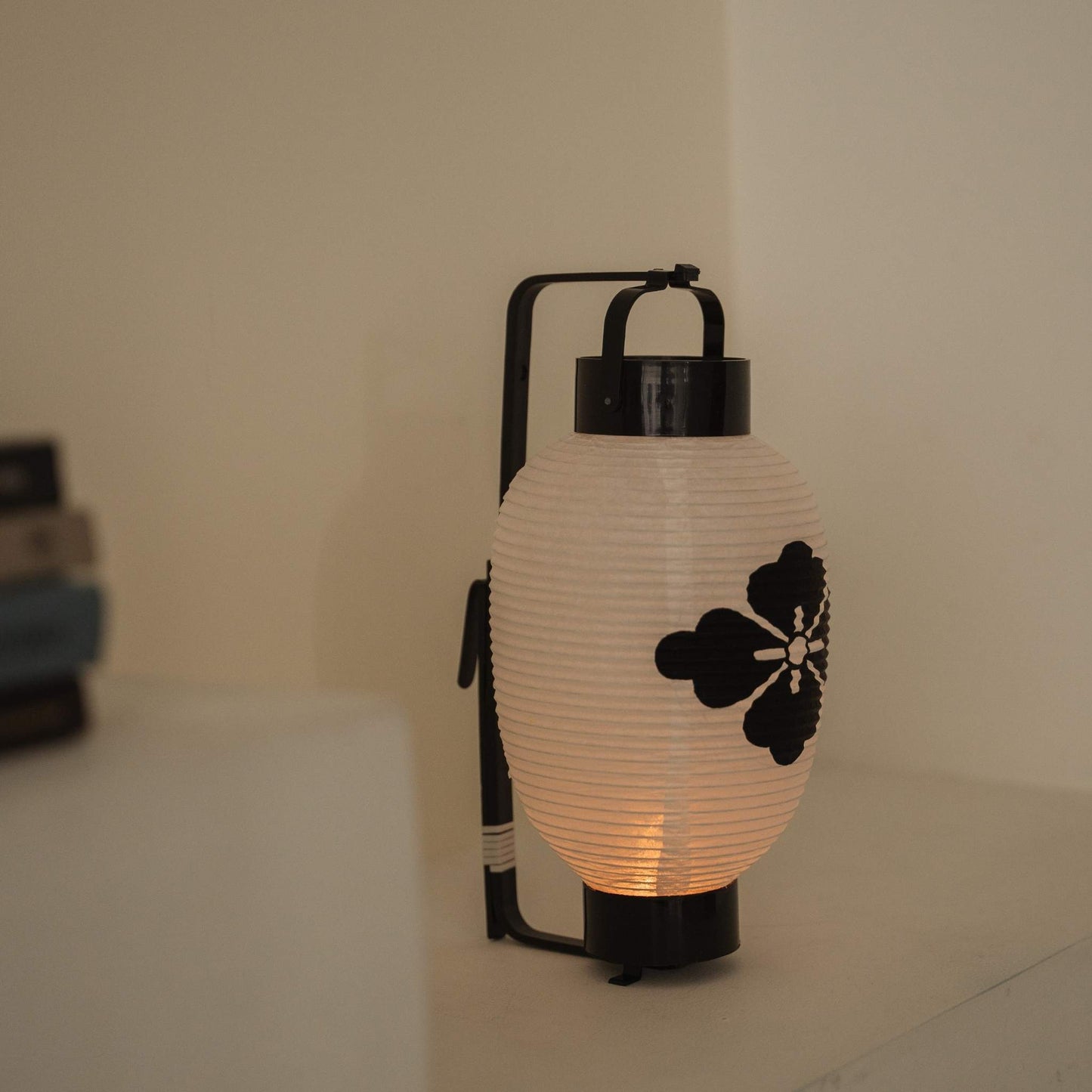 Lit Japanse papieren lantaarn met een zwart bloem-diamant-wapenschild, staand op een schone witte plank.