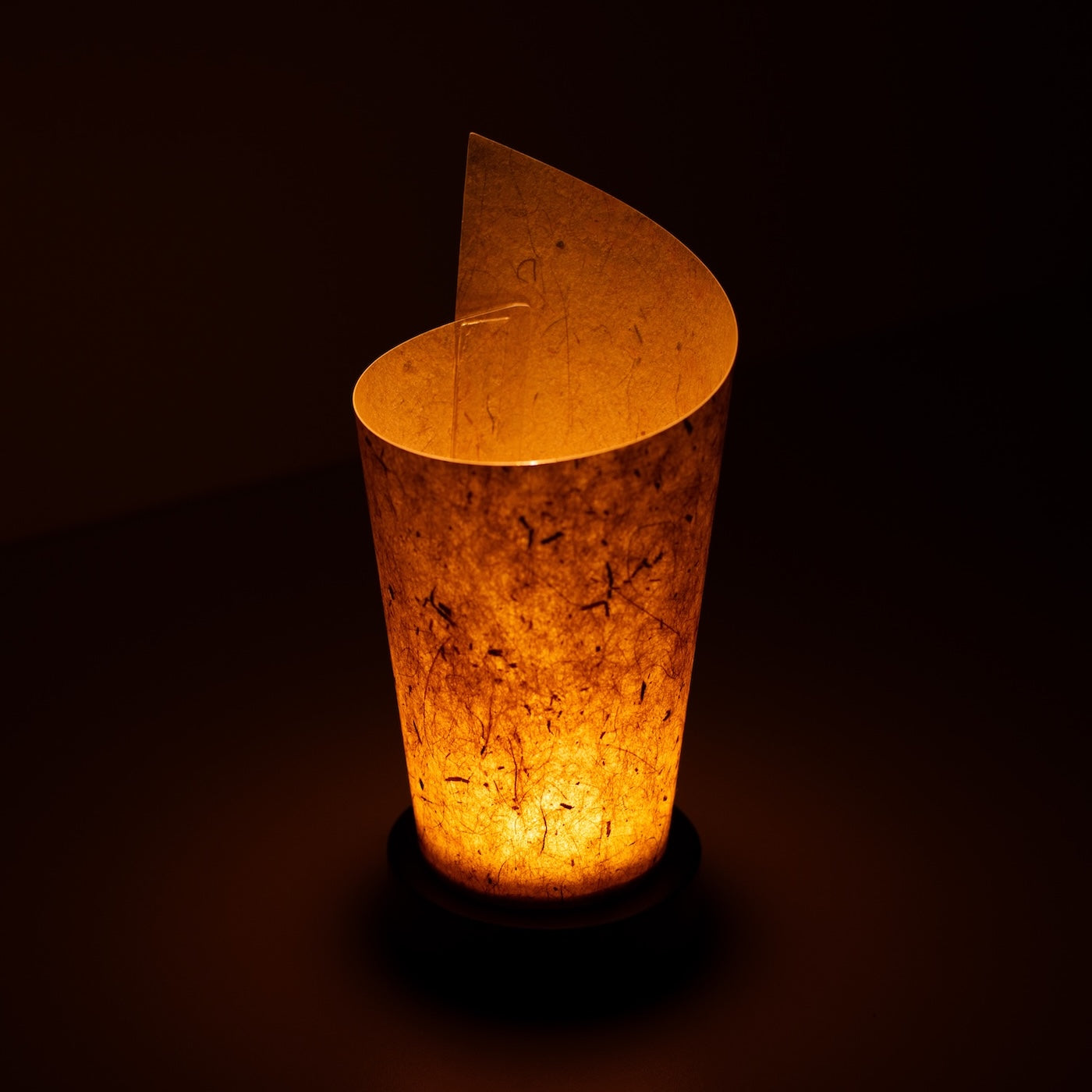 "Lampe de table japonaise en papier « Maki » écorce de cèdre, marron, papier Mino Washi - vue en plongée d'une lampe Japandi allumée montrant son design roulé."
