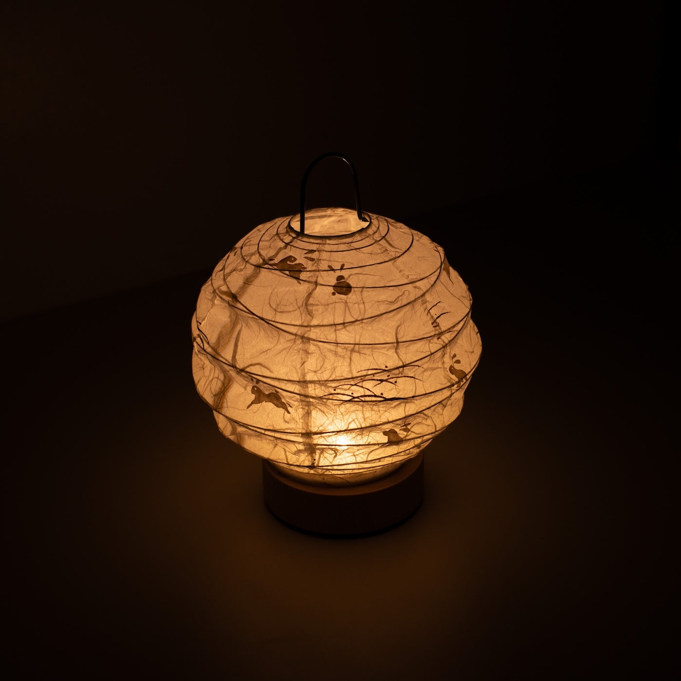 Japanese Paper Table Lamp "Yuhi" Rabbit, white, Mino Washi paper - high angle view of lit Japandi style lamp with wire handle.