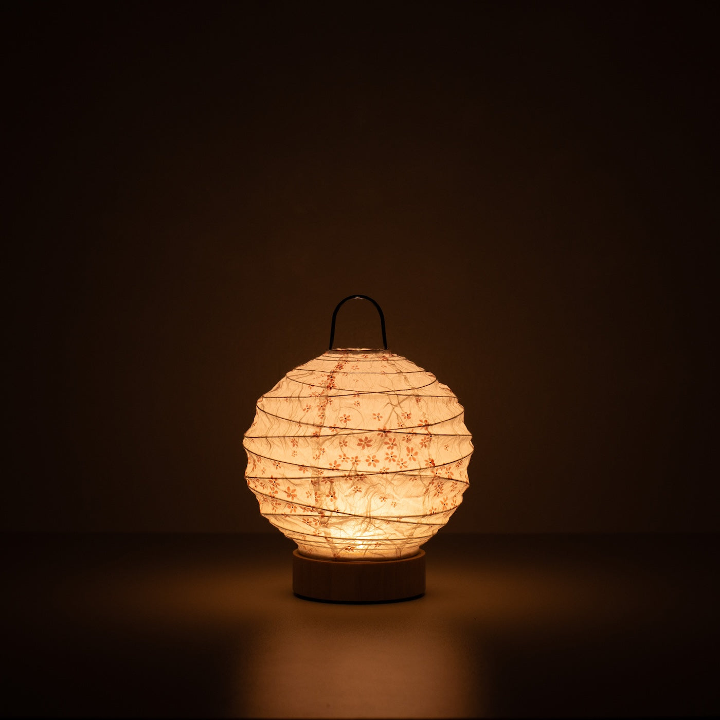 Japanese Paper Table Lamp "Yuhi" Sakura, white, Mino Washi paper - lit round paper lamp casting a warm glow in a dark room.
