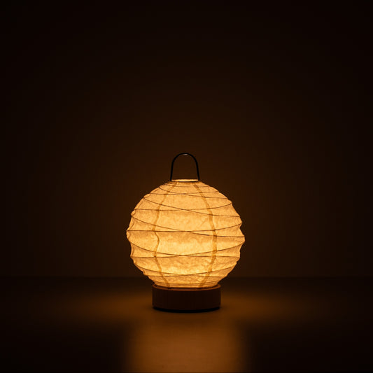 Japanese Paper Table Lamp "Yuhi", white, Mino Washi paper - lit round paper lamp casting a warm glow in a dark room.