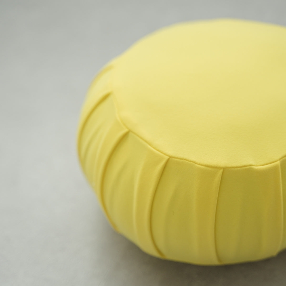Gros plan d'un coussin de méditation japonais (zafu) jaune mimosa, montrant son tissu plissé sur un sol moderne pour le yoga.