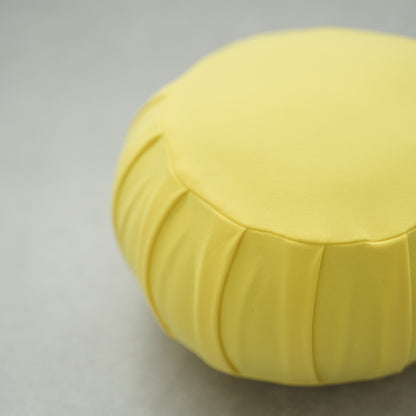 Gros plan d'un coussin de méditation japonais (zafu) jaune mimosa, montrant son tissu plissé sur un sol moderne pour le yoga.