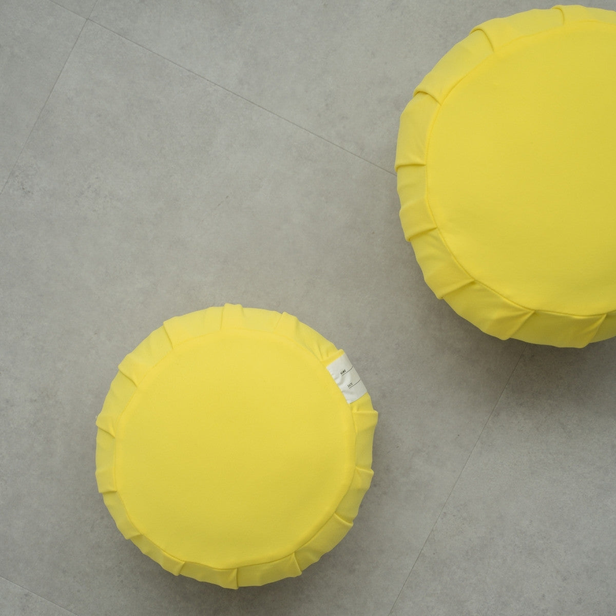 Deux coussins de méditation japonais (zafu) mimosa jaune sur un sol gris moderne, disposés pour un rituel zen familial partagé.