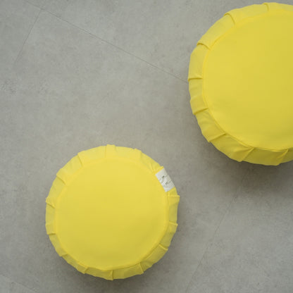 Deux coussins de méditation japonais (zafu) mimosa jaune sur un sol gris moderne, disposés pour un rituel zen familial partagé.