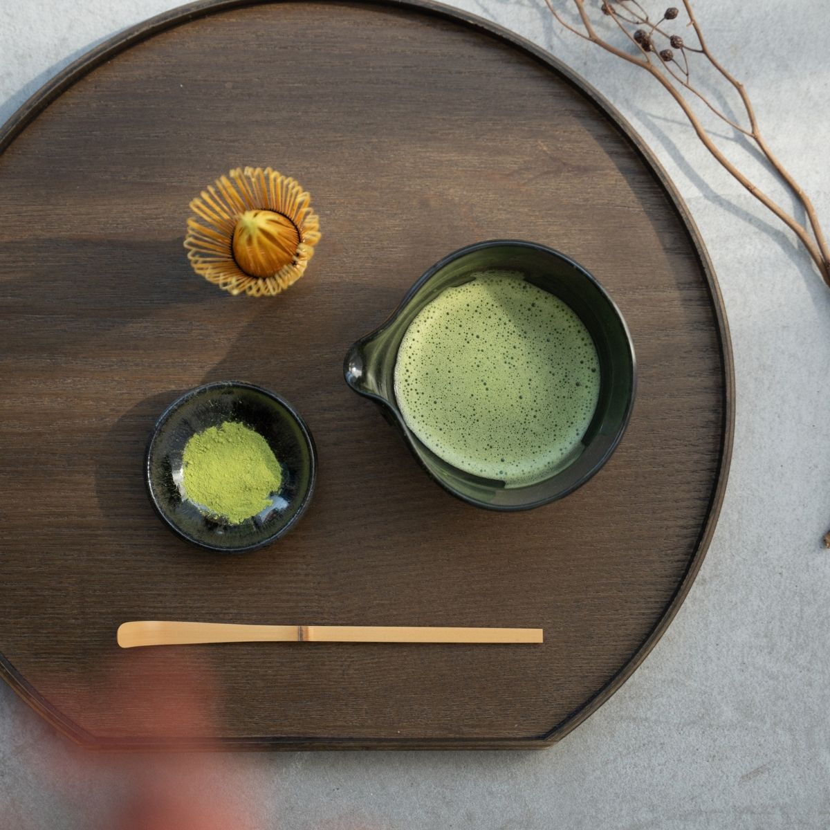 A spouted Japanese matcha bowl on a dark wood tray with a whisk and scoop for a mindful green tea ritual.