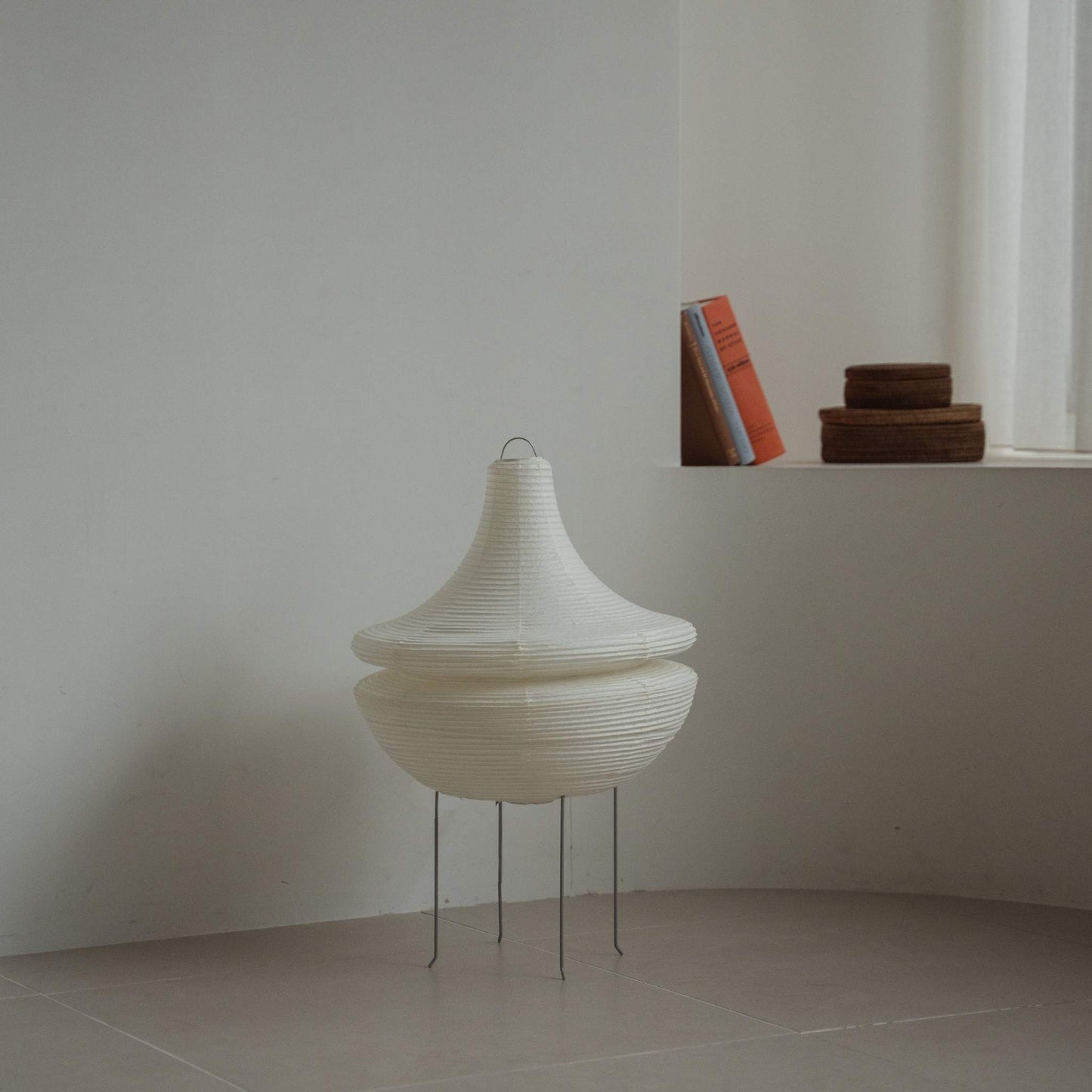"Lampe sur pied moderne en papier japonais Gemini 02 posée sur un sol carrelé dans une pièce blanche minimaliste avec des livres en arrière-plan"