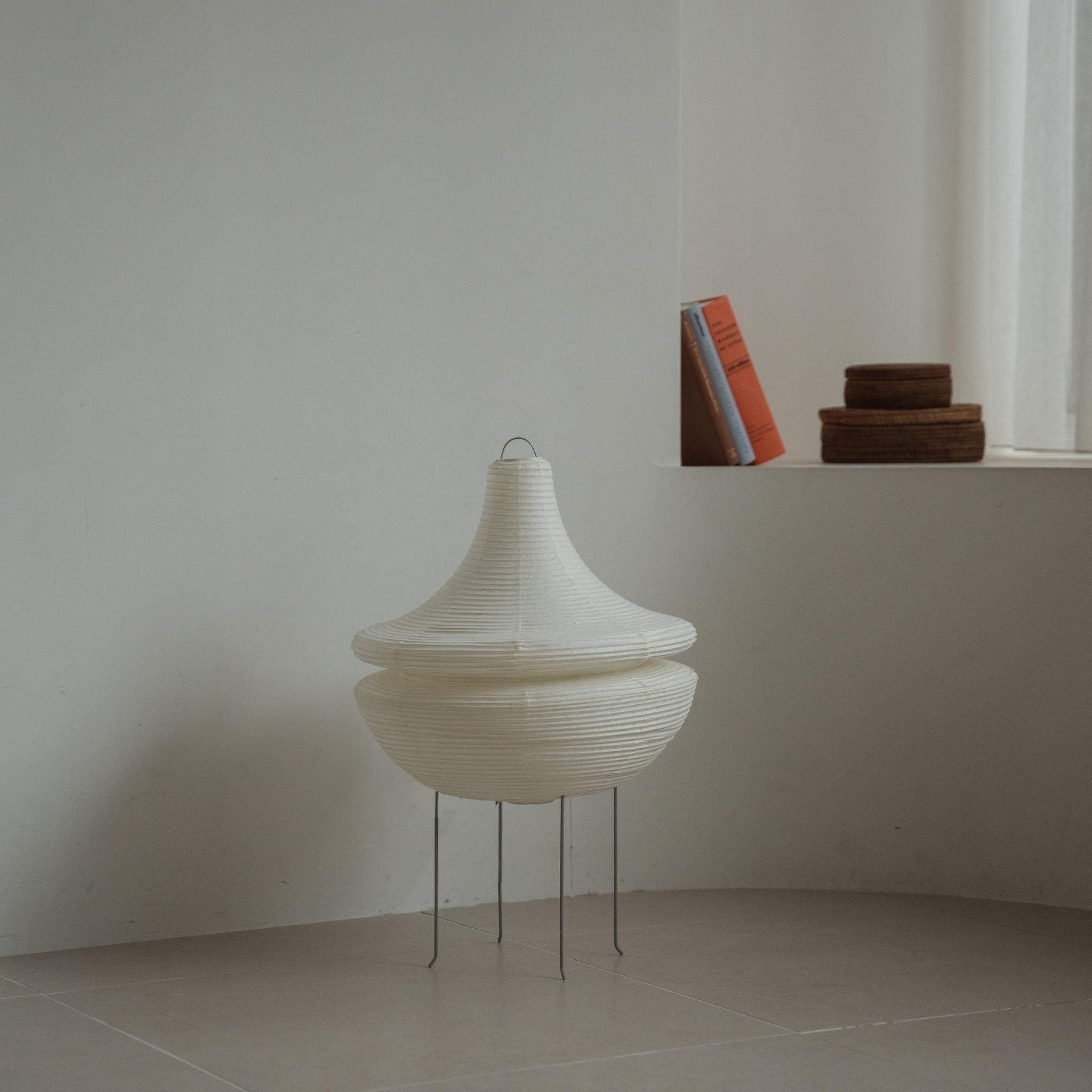 "Lampe sur pied moderne en papier japonais Gemini 02 posée sur un sol carrelé dans une pièce blanche minimaliste avec des livres en arrière-plan"