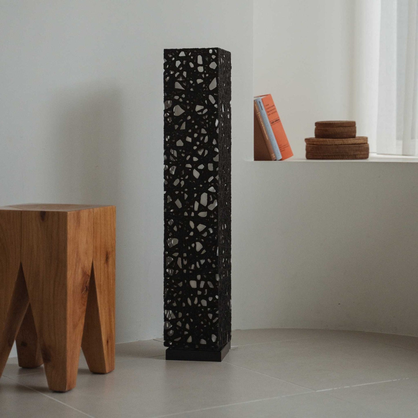"Lampe sur pied japonaise noire Me Look 01 éteinte dans une pièce blanche à côté d'un tabouret en bois et de livres."