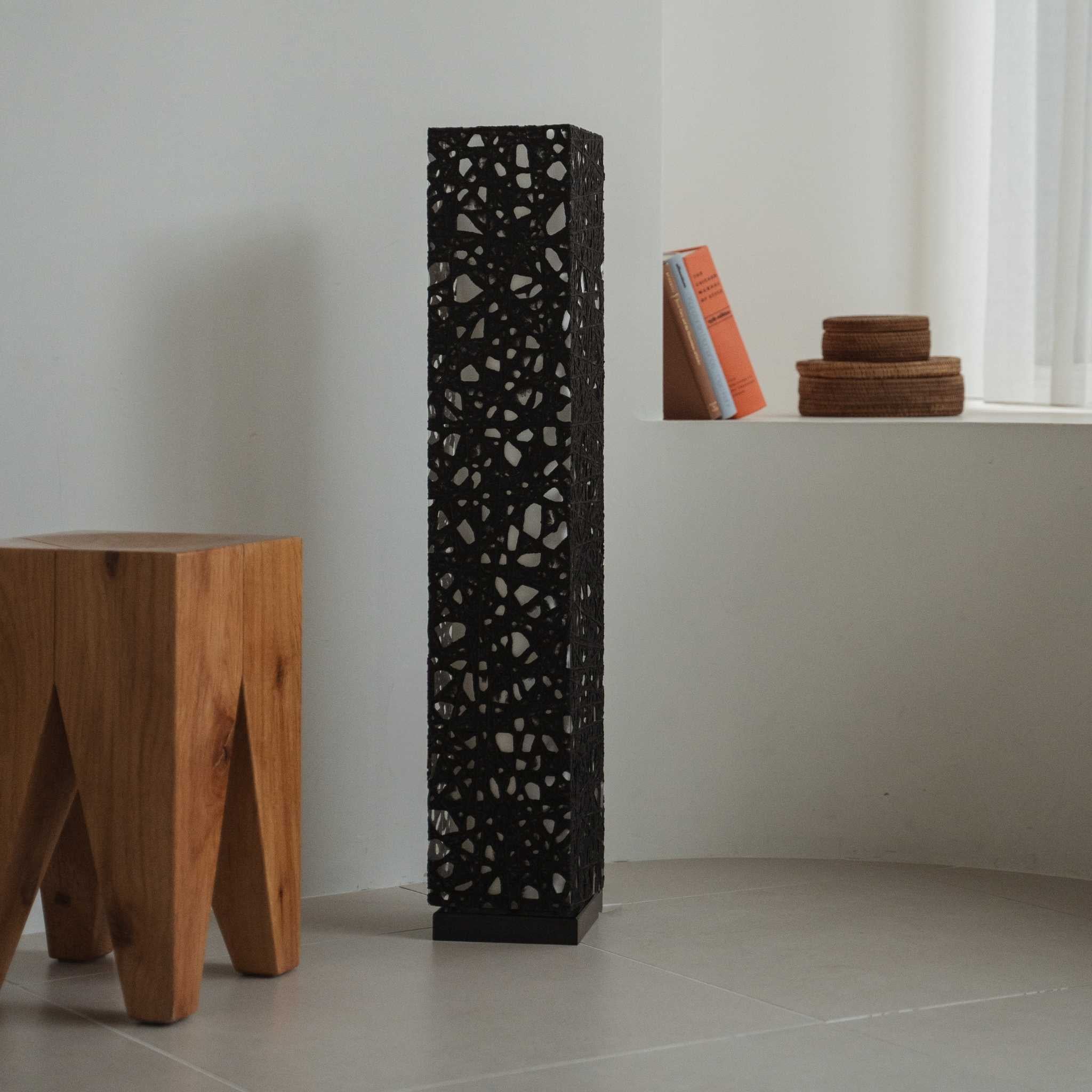 "Lampe sur pied japonaise noire Me Look 01 éteinte dans une pièce blanche à côté d'un tabouret en bois et de livres."