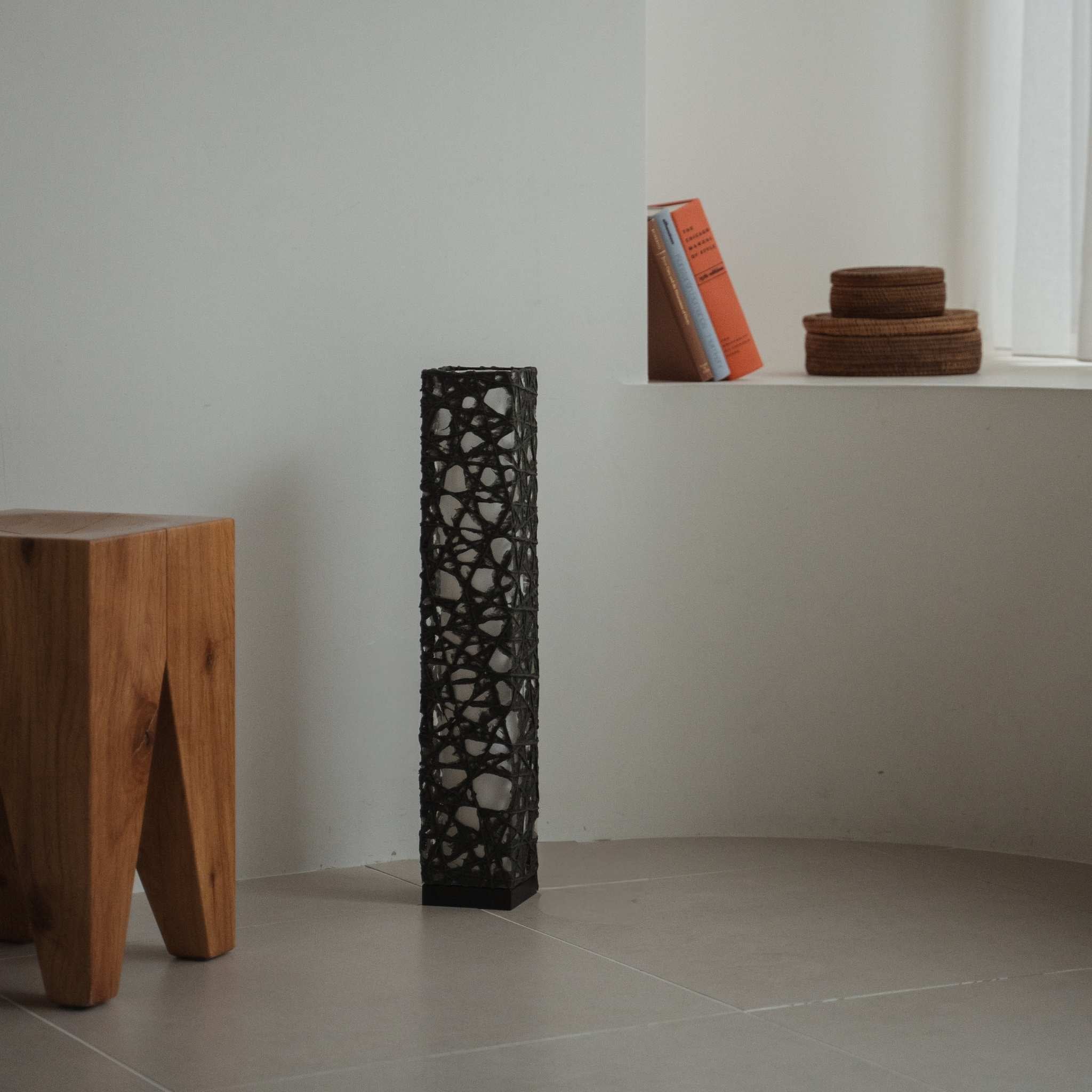 Lampe sur pied noire compacte Me Look 02, éteinte, sur un sol carrelé dans une pièce blanche minimaliste avec des livres.