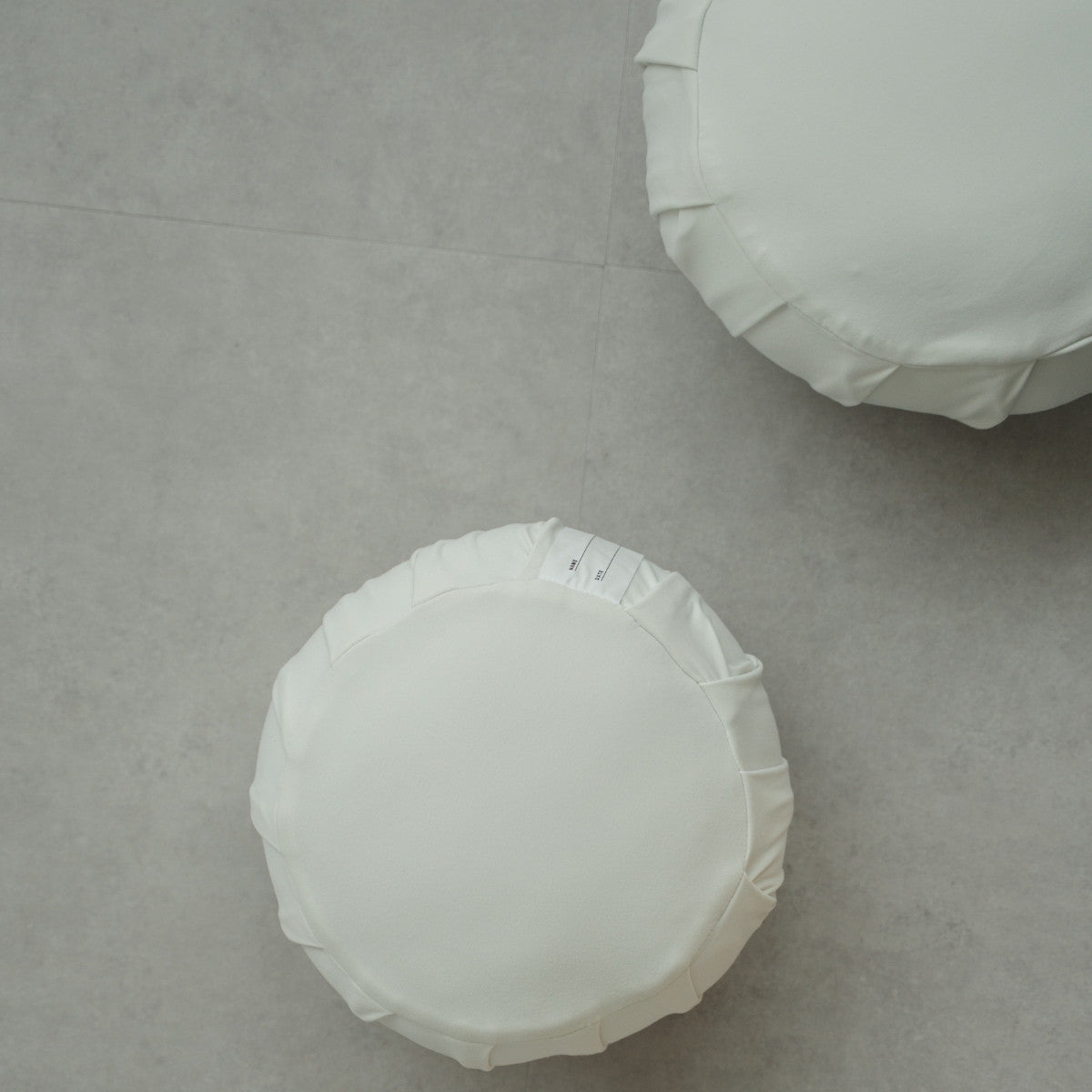 Deux coussins de méditation japonais blancs clair de lune (zafu) sur un sol gris moderne, prêts pour une routine de pleine conscience familiale.