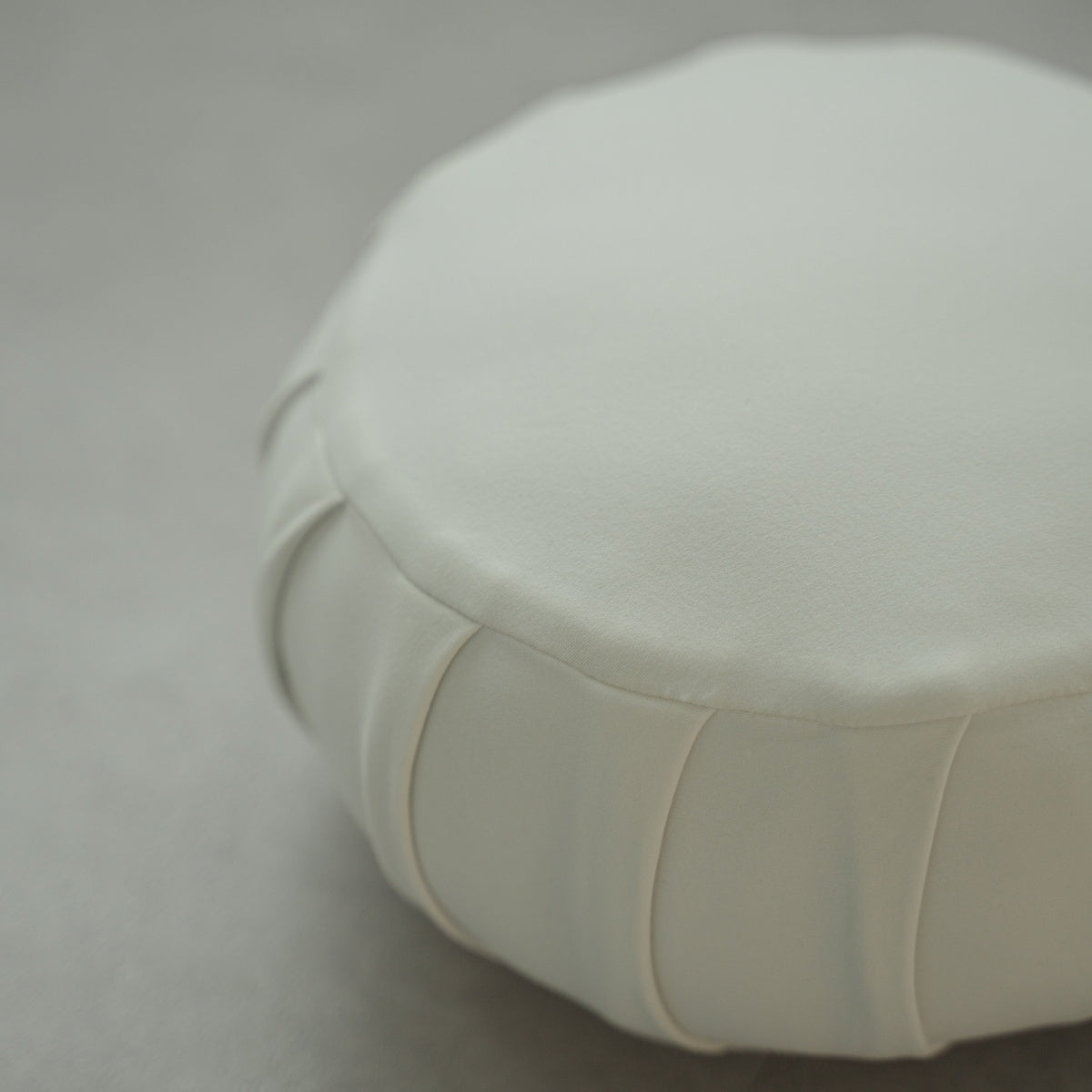 Gros plan d'un coussin de méditation japonais blanc clair (zafu) montrant les détails du tissu sur un sol moderne pour le yoga à domicile.
