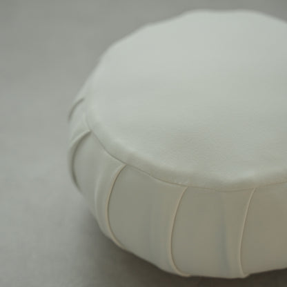 Gros plan d'un coussin de méditation japonais blanc clair (zafu) montrant les détails du tissu sur un sol moderne pour le yoga à domicile.