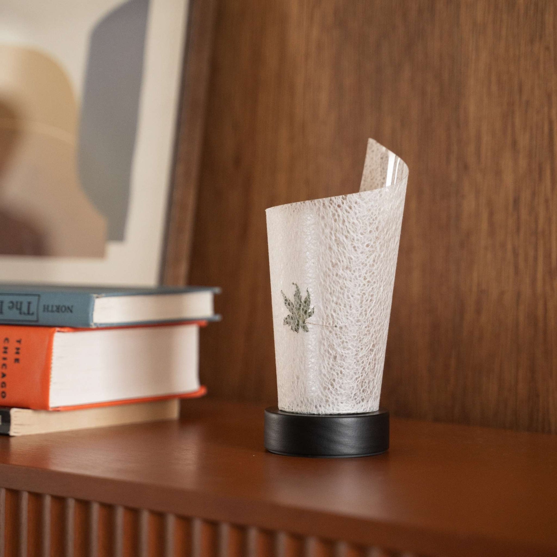 Gros plan d'une lampe de table japonaise en papier "Maki" non allumée, feuille d'érable, mettant en valeur ses marbrures naturelles et son esthétique wabi sabi sur une console.