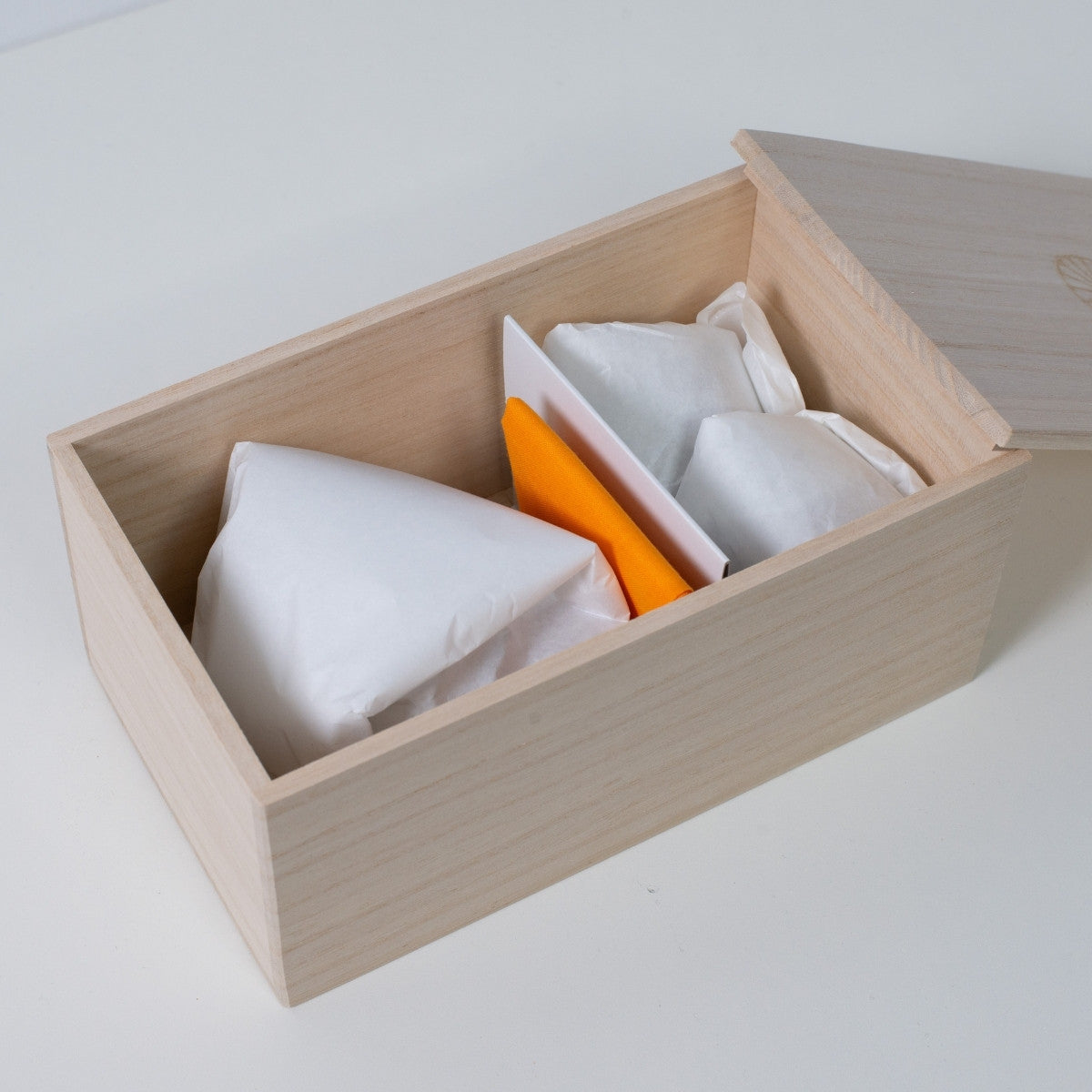 Open rectangular Ninshu's wooden box for a Japanese pottery sake set, showing wrapped vessels with a yellow cloth inside.