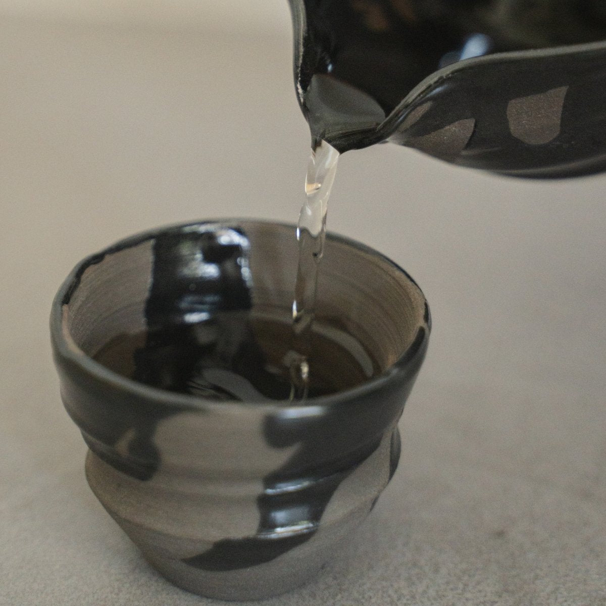 Sake hældes fra en Sumi Black japansk Katakuchi sakekaraffel, i en matchende sakekop (ochoko), til servering af premium sake.