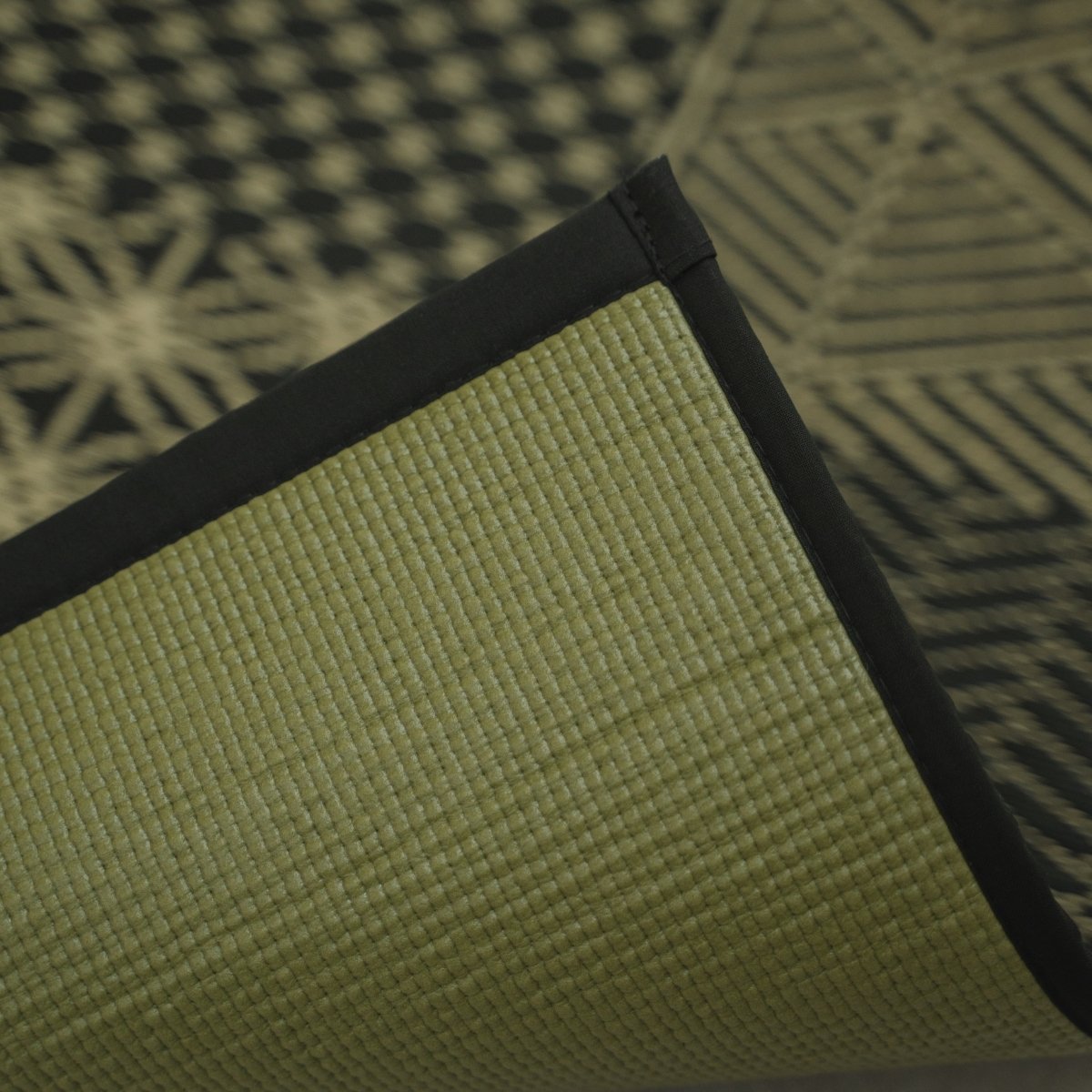 Hoek van de Japanse Tatami Yoga Matras "Ed Plain" Zwart opgetild om de getextureerde PVC-achterkant en zwarte rand te tonen.