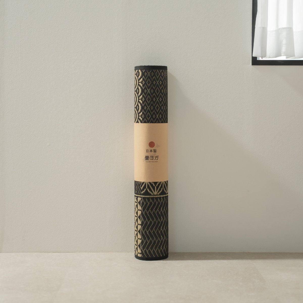 Rolled Japanse Tatami Yogamat "Ed Plain" Zwart staand bij een witte muur, klaar voor je dagelijkse mindfulness oefening.