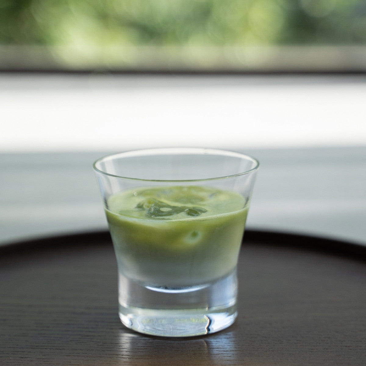 Iced matcha latte in a glass on a dark wood tray for a refreshing break with a green background.