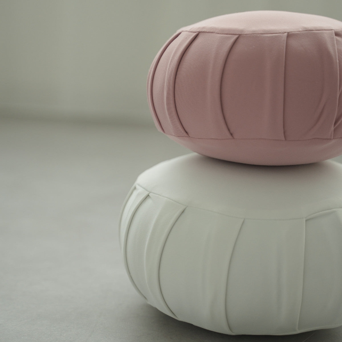 Rose og måneskin hvid japansk meditationspude zafu, placeret på et gråt gulv klar til en familie zen-rutine.