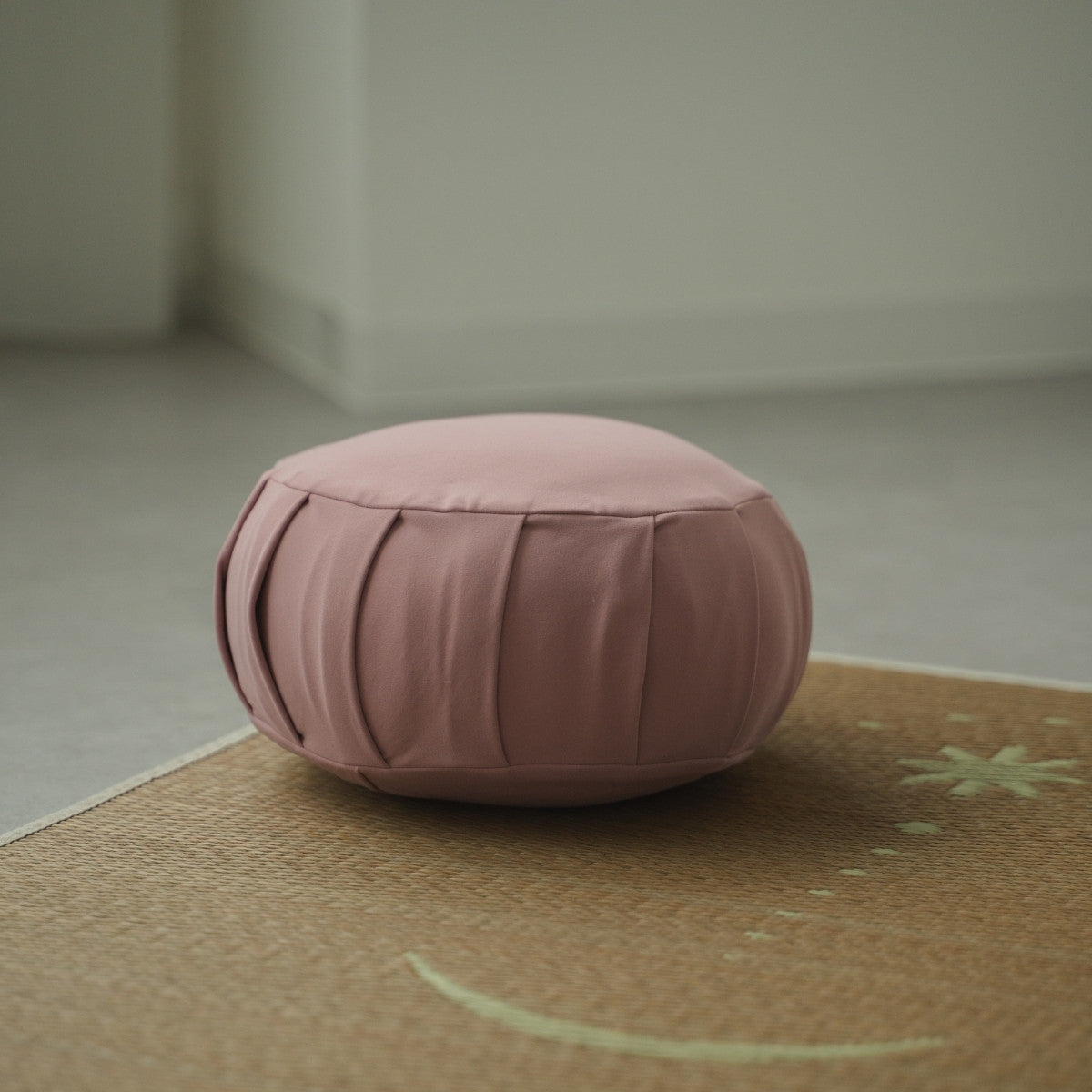 Rose japansk meditationspude zafu, placeret på en vævet måtte i et roligt rum til et dagligt zen-ritual.