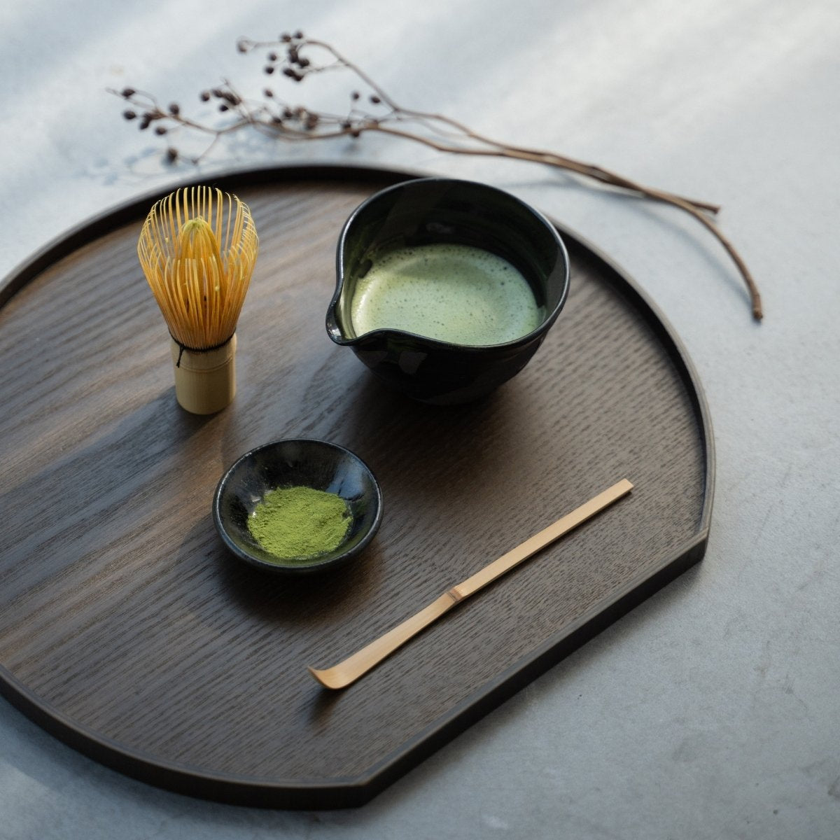 A Japanese matcha bowl with spout on a dark wood tray, part of a serene daily tea ceremony on a concrete table.