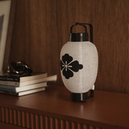 Traditionele Japanse papieren lantaarn met bloemenruit-wapenschild, geplaatst naast boeken op een houten console tafel.